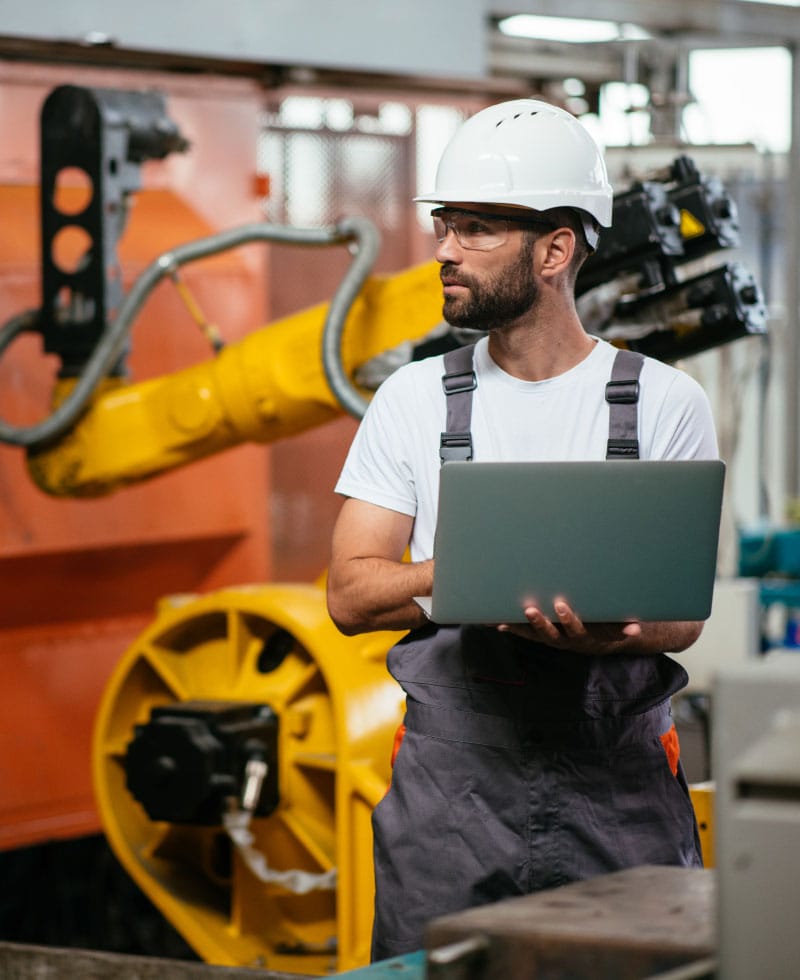 Travailleur dans une usine utilisant un ordinateur portable à proximité de machines robotisées