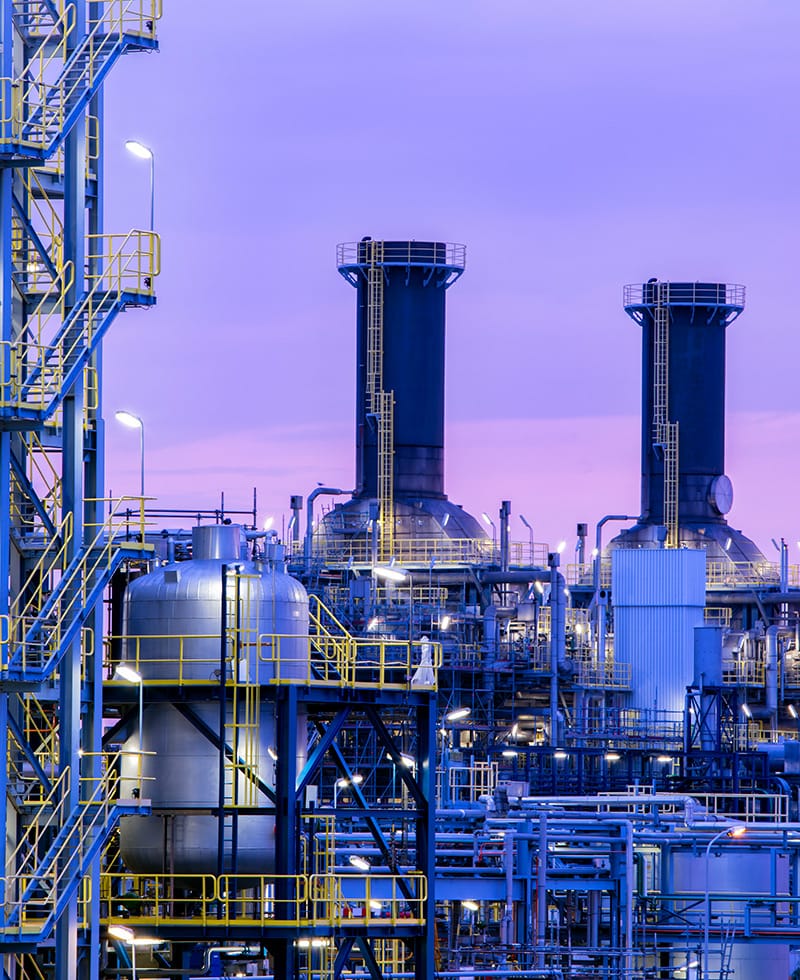 Grande installation industrielle avec des tours, des réservoirs et des tuyaux au crépuscule.