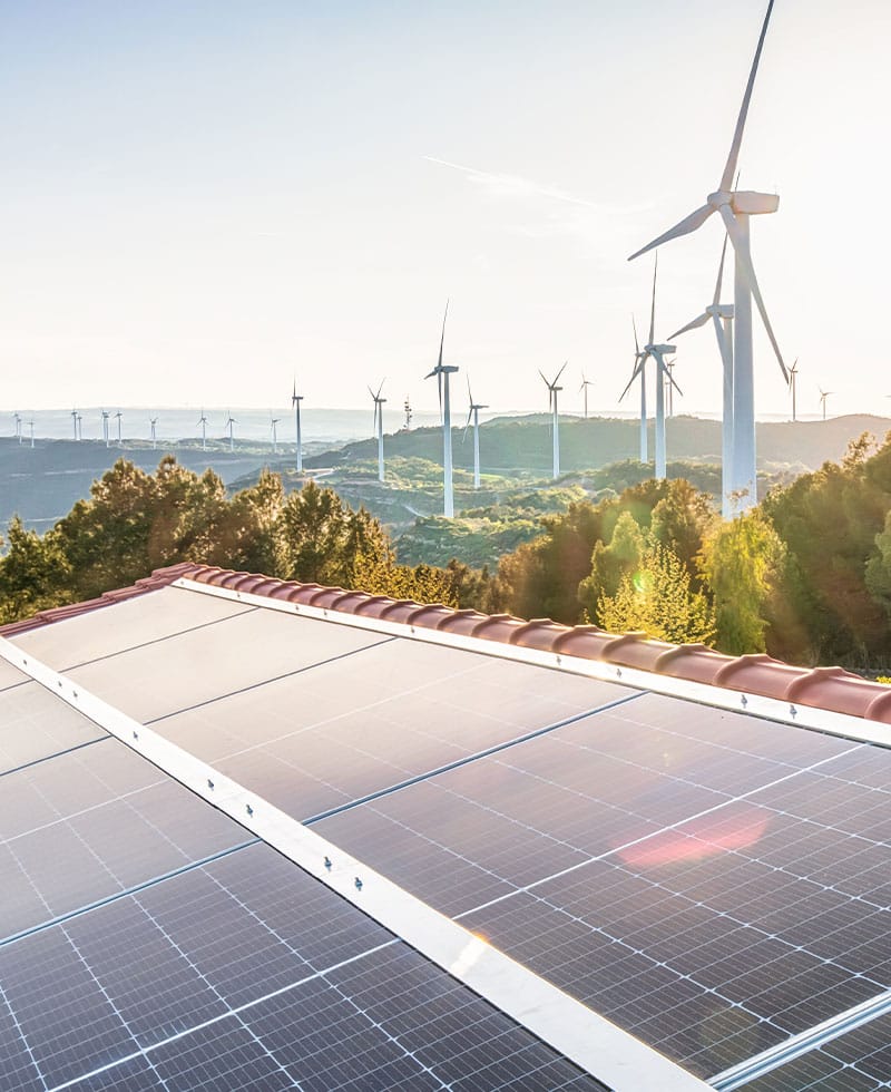 Des panneaux solaires installés sur les toits et des éoliennes à flanc de colline, illustrant l'intégration des ressources énergétiques distribuées (RED).