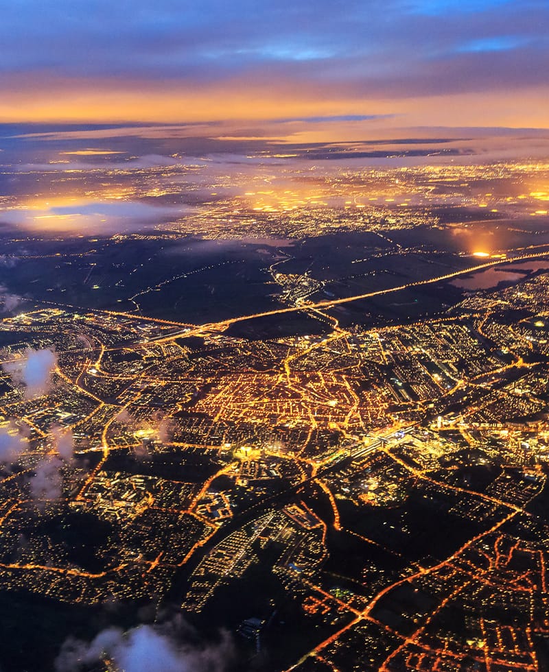 Vue aérienne nocturne du réseau électrique et du réseau routier illuminés d'une ville, illustrant l'automatisation des réseaux intelligents.
